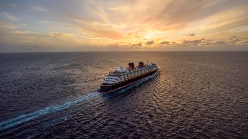 A Disney Cruise Line ship sails along in tranquil, open water, with a beautiful sunset in the background