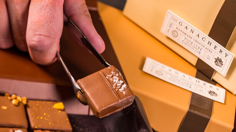 A chocolatier lifting a ganache square with tongs at The Ganachery