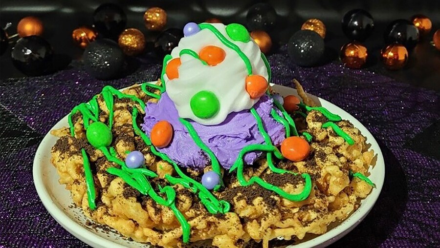 On plate is Foolish Mortal Funnel Cake, topped with crumbled Oreo, vanilla ice cream, caramel drizzle and M and M Ghouls Mix