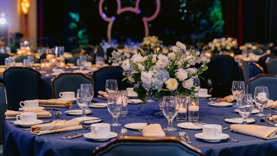Un lugar para eventos con salón de baile con mesas de comedor, sillas, arreglos florales y cubiertos