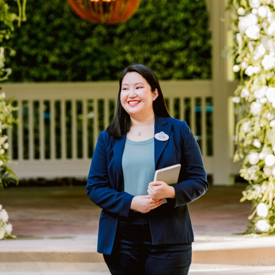 Un planificador de eventos de Disney sosteniendo un cuaderno y parándose frente a una glorieta con un arco floral