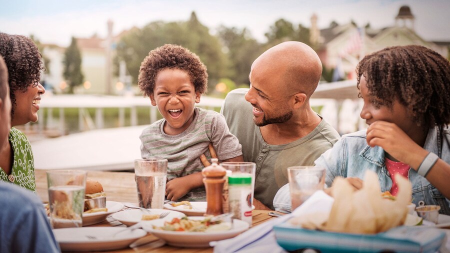 A family of 4 smiling as they dine outdoors at a Disney restaurant