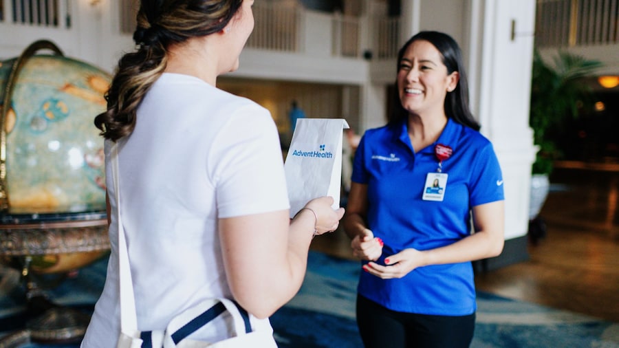 A Guest receiving a prescription delivery from an Advent Health staff member in a Resort hotel lobby