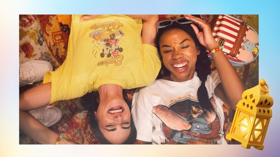 Two Guests laying on the ground with their heads facing opposite directions while wearing Disney shirts