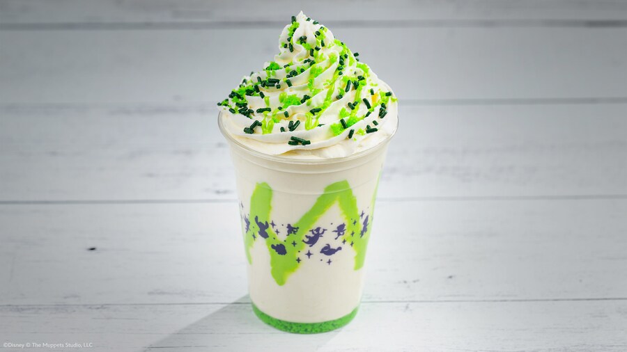A milkshake topped with whipped cream and covered in sprinkles, served in a cup featuring Muppets themed silhouettes