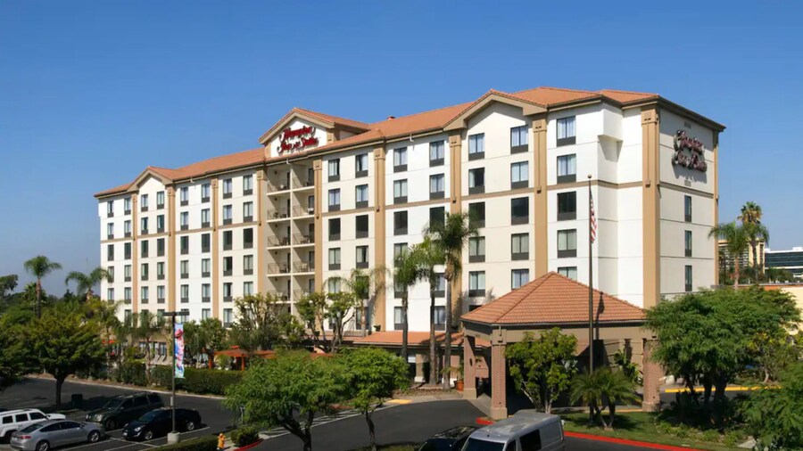 Un hotel de 7&nbsp;pisos junto a un área de estacionamiento y árboles, con un marquesina que dice “Hampton Inn & Suites”