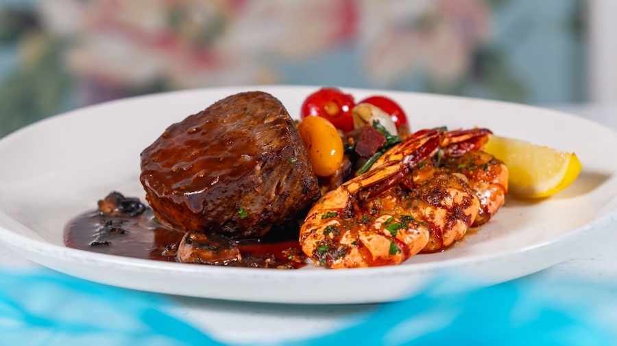 A steak topped with sauce plated next to shrimp and vegetables, available during Disneyland After Dark 70 Years of Favorites