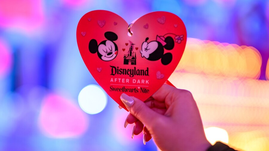 Hands holding a Disneyland After Dark Sweethearts’ Nite commemorative heart shaped credential featuring artwork of Minnie Mouse giving Mickey Mouse a kiss on the cheek