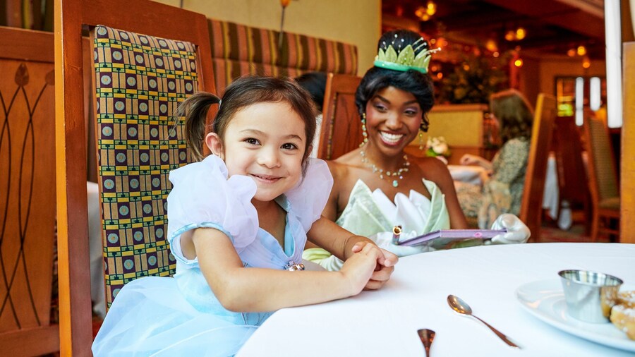 A young girl in a princess dress sitting at a dining table with Princess Tiana