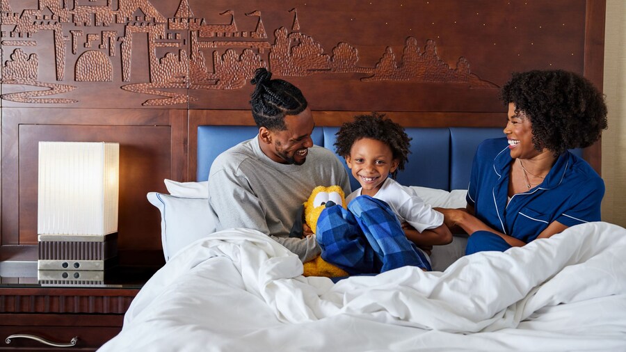 Two parents and their child smiling and playing in bed in a hotel room	