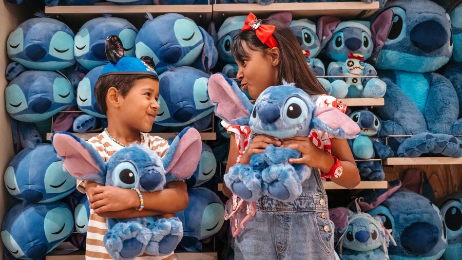 Two children holding Stitch plush toys in front of a shelf of Stitch merchandise