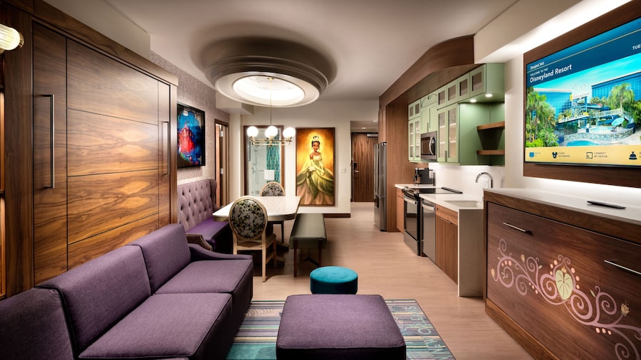 A hotel villa living area with a kitchen, couch, dining table, TV and 'The Princess and the Frog' themed artwork