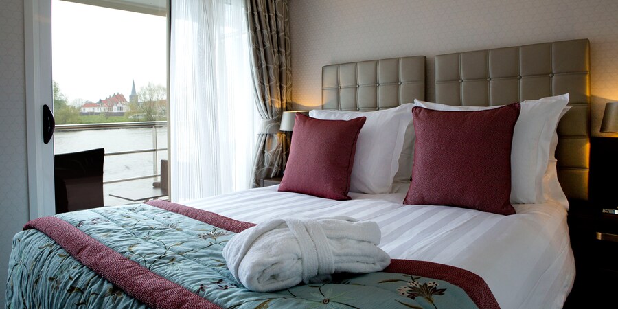 A Category BB room, featuring a double bed and a table with chairs, outside of a sliding balcony door. A Category BB room, featuring a double bed and a table with chairs, outside of a sliding balcony door.