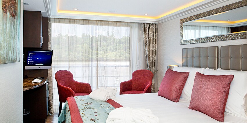 A Category C room, featuring a double bed, two club chairs and a sliding balcony door.