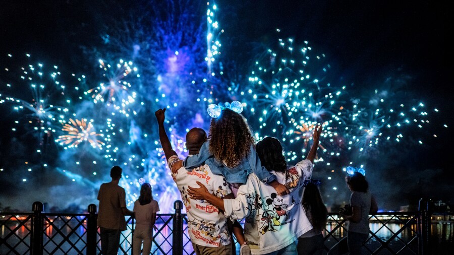 Two parents hold their young daughter as they watch a fireworks show over Epcot