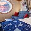 Stateroom with large porthole, sofa and coffee table, dividing curtain, and queen size bed