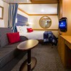 Stateroom with sofa and coffee table, dividing curtain, bed, round mirror on wall, built in desk with TV