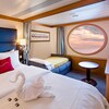 Stateroom with bed, dividing curtain, turned down sofa bed, large porthole, built in dresser and TV