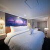 A Deluxe Oceanview Stateroom with a queen size bed, sofa bed, 2 nightstands, 2 wall sconces, a TV, vanity dresser, wall art and a privacy curtain