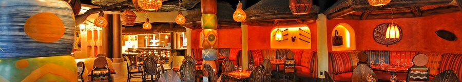 Faroles colgantes sobre mesas con sillas y decoraciones en la pared de diseño tribal