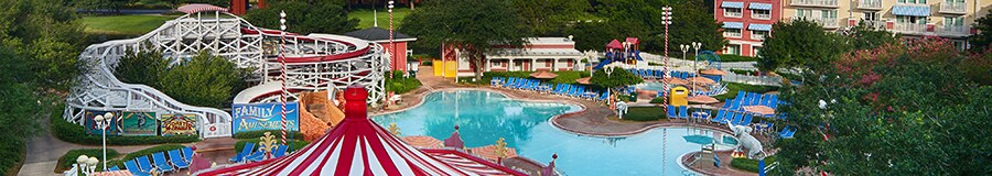 El área de la piscina de Disney's BoardWalk Inn con 2 edificios de varios pisos, árboles frondosos, un snack bar con forma de carrusel y un tobogán acuático con un diseño que se asemeja a una montaña rusa