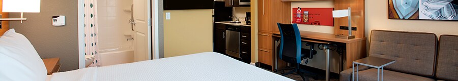 Una cama King Size en una habitación de hotel bien amueblada, con un baño y una cocina en segundo plano