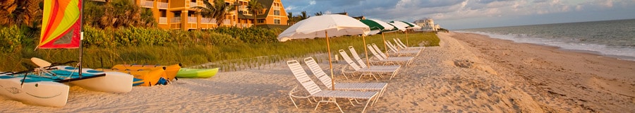 A beach with lounge chairs, umbrellas and rental boats, with the Resort behind