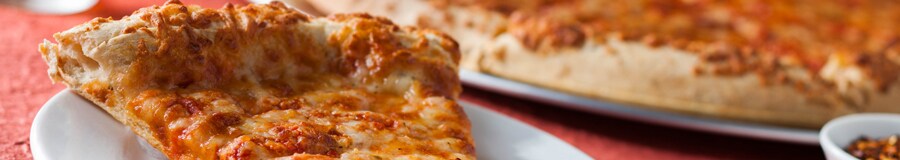 A cheese pizza with crunchy crust, plated directly from an oven pan, next to toppings and a tall drink
