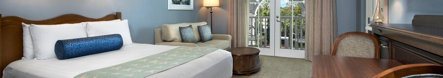Um quarto com um sofá, uma luminária, uma cadeira, um baú, cortinas e acesso à sacada