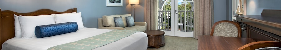 Une pièce avec un canapé, une lampe, une chaise, un coffre, des rideaux et un accès au balcon