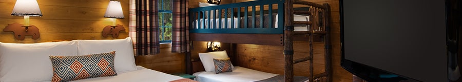 A flat screen TV, a queen size bed, 2 decorative sconces and a set of bunk beds