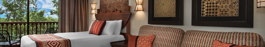 Un canapé, coussins décoratifs, 3 œuvres d’art murales, 2 appliques, un lit et un balcon donnant sur une savane luxuriante