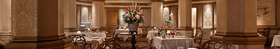 Salão de jantar formal no Victoria & Albert's, com um buquê de flores, quadros e mesa posta com belas porcelanas