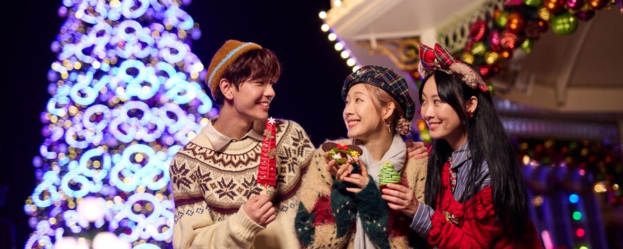 Three people by a lit Christmas tree at night.