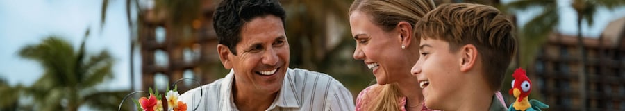 A dad, a mom and their 2 young daughters relaxing on a beach area in front of Aulani, A Disney Resort and Spa