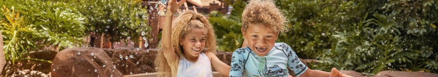 Two smiling children riding an inner tube in the lazy river at Aulani, A Disney Resort & Spa