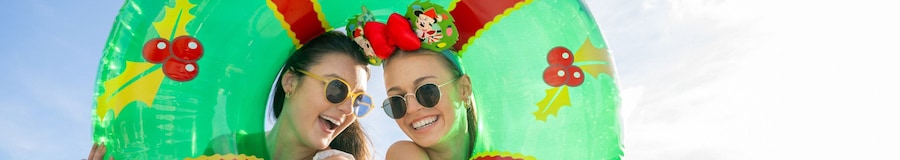 Two women peeking through and embracing an inner tube decorated to look like a Christmas wreath