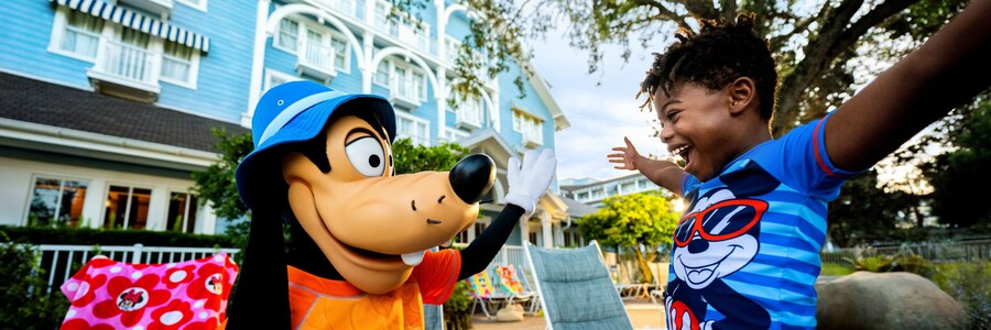 A child smiling in excitement as they greet Goofy while sitting near the pool at Disney’s Beach Club Resort