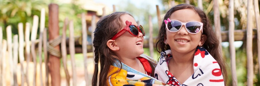 2 filles enveloppées dans des serviettes de plage portant des lunettes de soleil tout en se serrant l’une l’autre dans les bras
