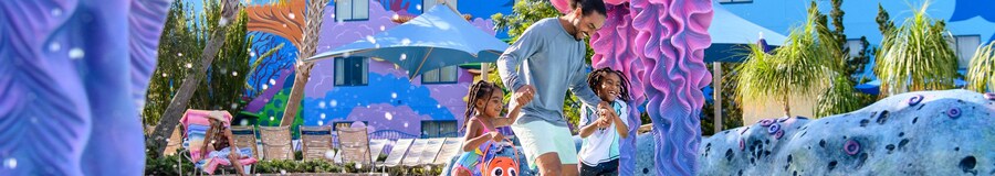 Un padre jugando con sus 2 hijas en la piscina Big Blue Pool en Disney's Art of Animation Resort 