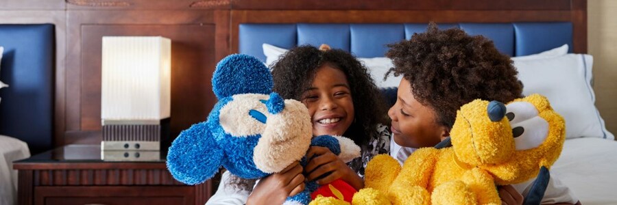 Dos niños jugando en una cama con un peluche de Mickey Mouse y Pluto