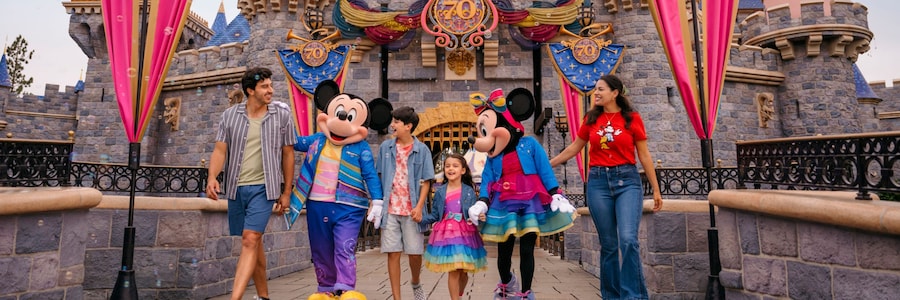 Family walking with Mickey and Minnie Mouse in front of the Disneyland castle during the 70th anniversary celebration