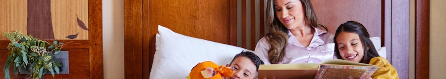 A mother reading to her 2 children in bed at Disney’s Grand Californian Hotel & Spa