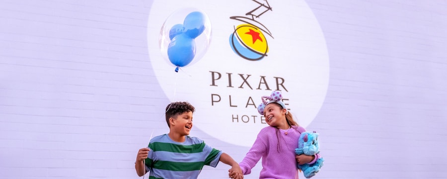 At Pixar Place Hotel, 2 kids skip together while one child holds a balloon and the other child holds a plush