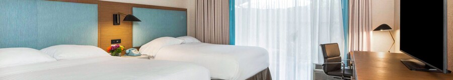 A room at The Anaheim Hotel with a dresser, desk, TV, nightstand, 2 chairs and 2 beds