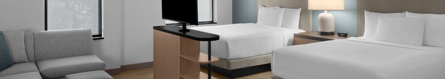 The Studio Kitchen Suite, with an L shaped couch and ottoman facing a flat screen TV, and 2 queen beds