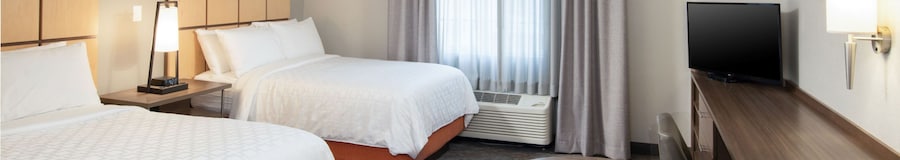 Una suite de un dormitorio con cama Queen Size de Candlewood Suites Anaheim Resort Area con una cama, 2 mesas de noche, 2 lámparas y cuadros en las paredes