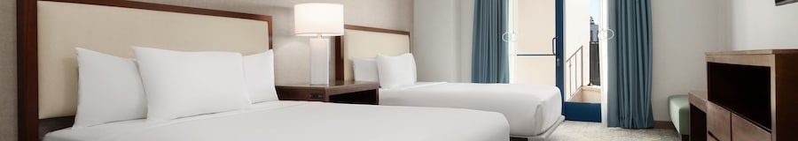 A hotel bedroom with 2 queen size beds, nightstand, TV, dresser and a glass door with balcony access