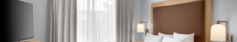 A hotel resort suite bedroom with a desk, dresser, bed and nightstand