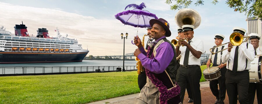 A man in cheery attire with a fluffy parasol leads a small band of musicians past a Disney cruise ship